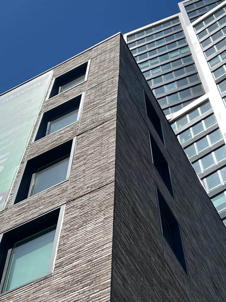 Looking up at the corner of The Maven's brick facade. A building and the sky are in the background.
